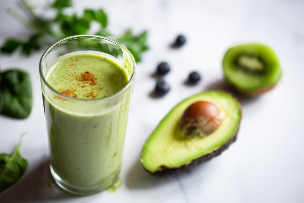 Auf einem Tisch steht ein grüner Smoothie aus Avocado und Kiwi.
