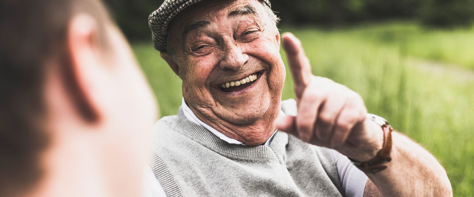 Ein älterer Mann erhebt lachend seinen Zeigefinger.