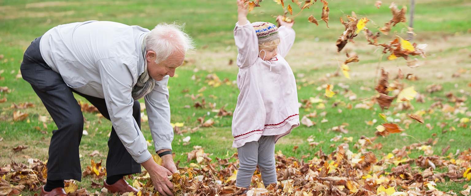 Ein alter Mann und ein Kleinkind werfen Herbstlaub in die Luft.