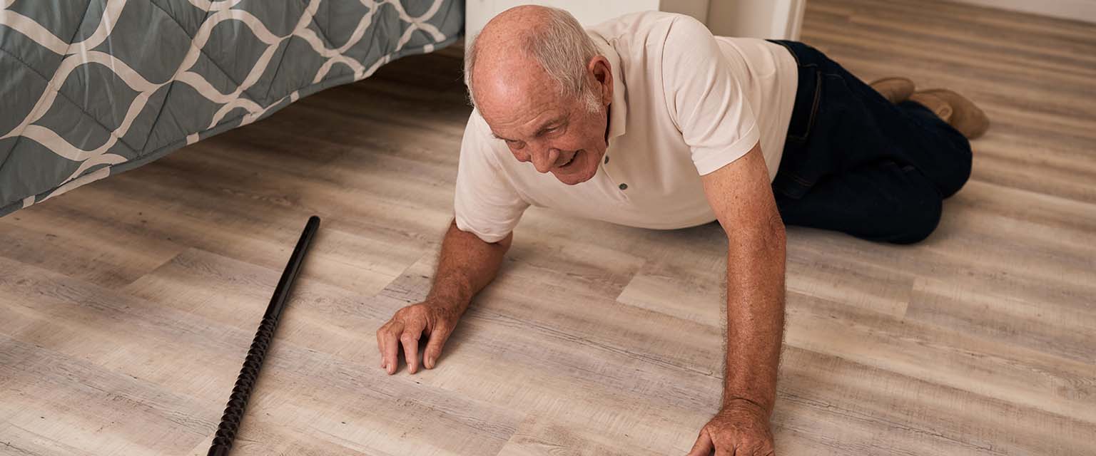 Ein alter Mann liegt im Schlafzimmer am Boden, ein Gehstock liegt vor ihm.