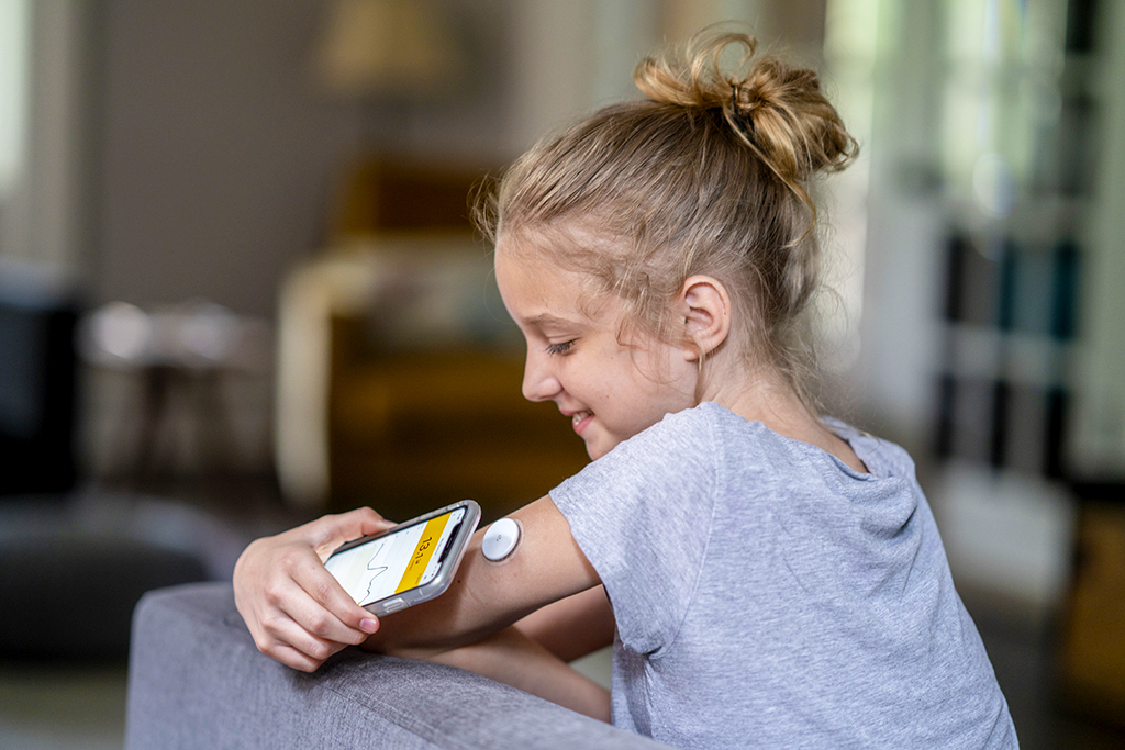 Ein Mädchen hält ihr Smartphone an den Oberarm. Dort befindet sich ein Sensor zur Blutzuckerbestimmung.