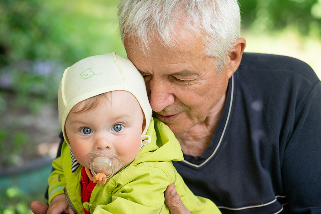 Ein alter Mann schmiegt sein Gesicht an den Körper eines Babys. Es schaut in die Kamera.