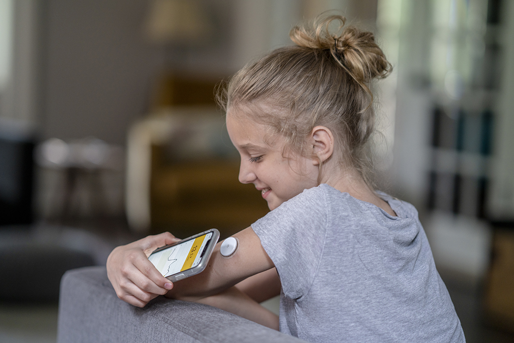 Ein Mädchen hält ihr Smartphone an den Oberarm. Dort befindet sich ein Sensor zur Blutzuckerbestimmung.