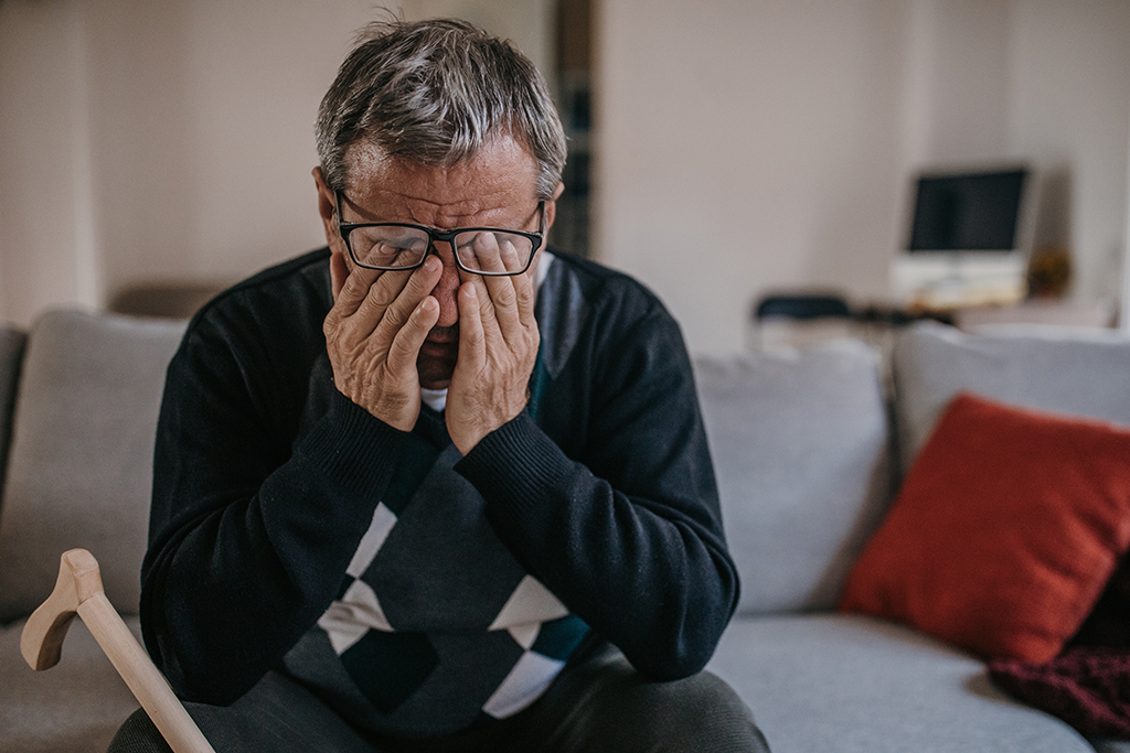 Ein älterer Mann reibt sich auf dem Sofa sitzend die Augen.