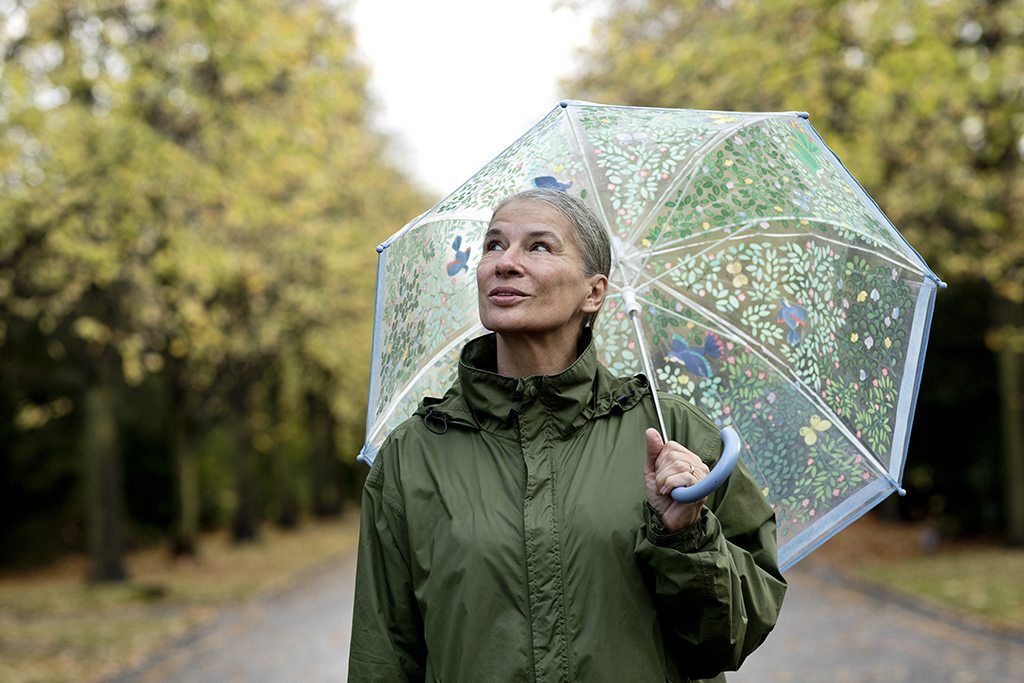Eine ältere Frau mit einem Regenschirm schaut nachdenklich in Richtung Himmel.