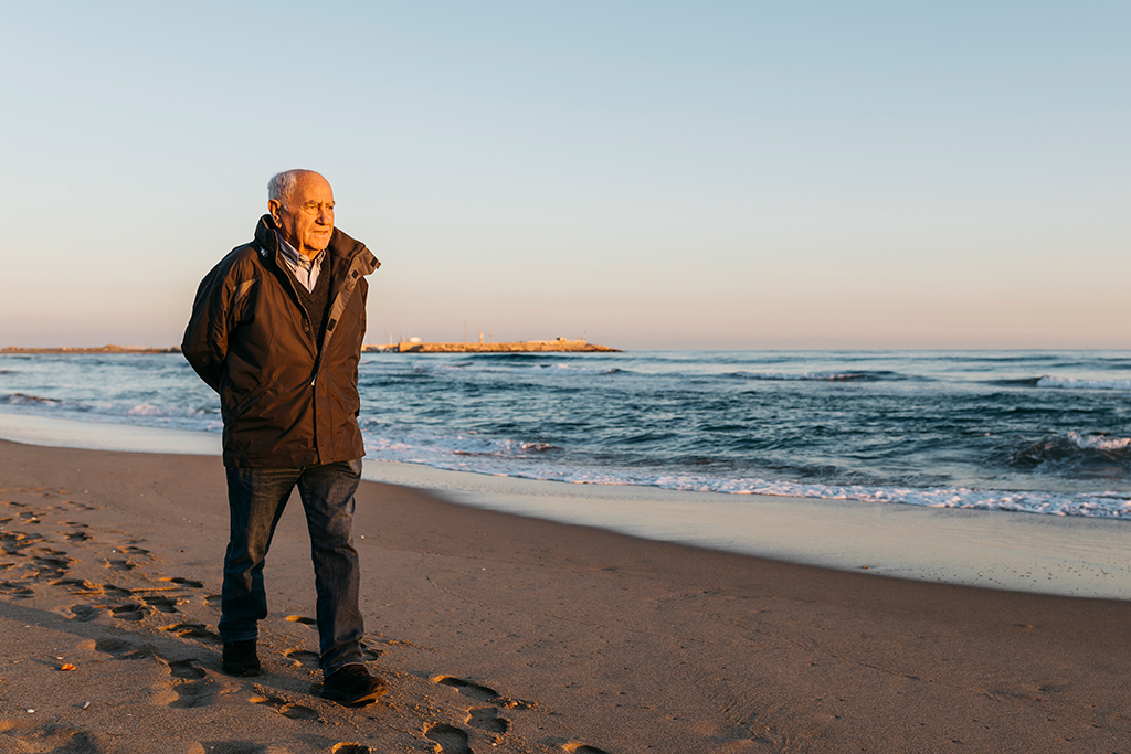 Ein älterer Herr geht allein am Strand spazieren.