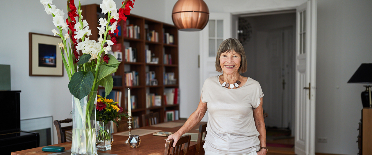 Eine Seniorin steht stolz und glücklich an ihrem Esstisch.